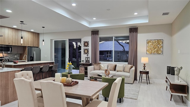 dining room featuring a raised ceiling, sink, and light hardwood / wood-style flooring