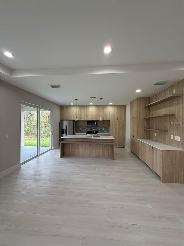 kitchen featuring pendant lighting, appliances with stainless steel finishes, sink, and a center island with sink