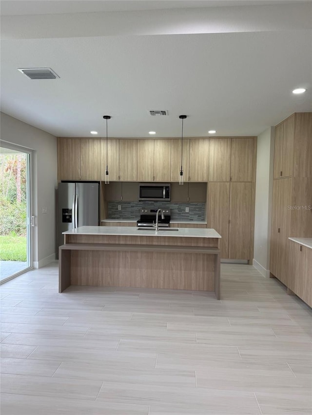 kitchen with a kitchen island with sink, sink, hanging light fixtures, decorative backsplash, and appliances with stainless steel finishes