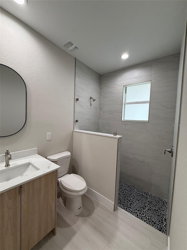 bathroom with a tile shower, vanity, toilet, and wood-type flooring