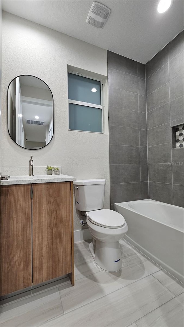 full bathroom with tiled shower / bath, vanity, toilet, and a textured ceiling