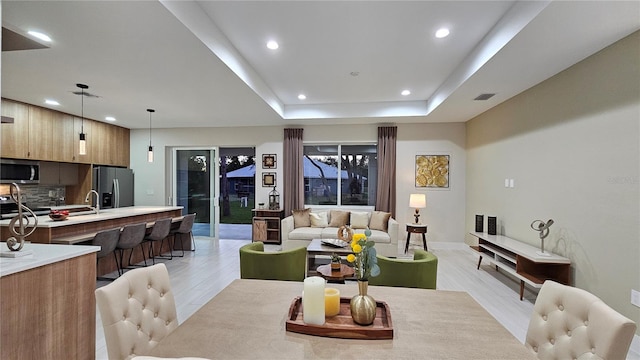 living room with sink, a raised ceiling, and light wood-type flooring