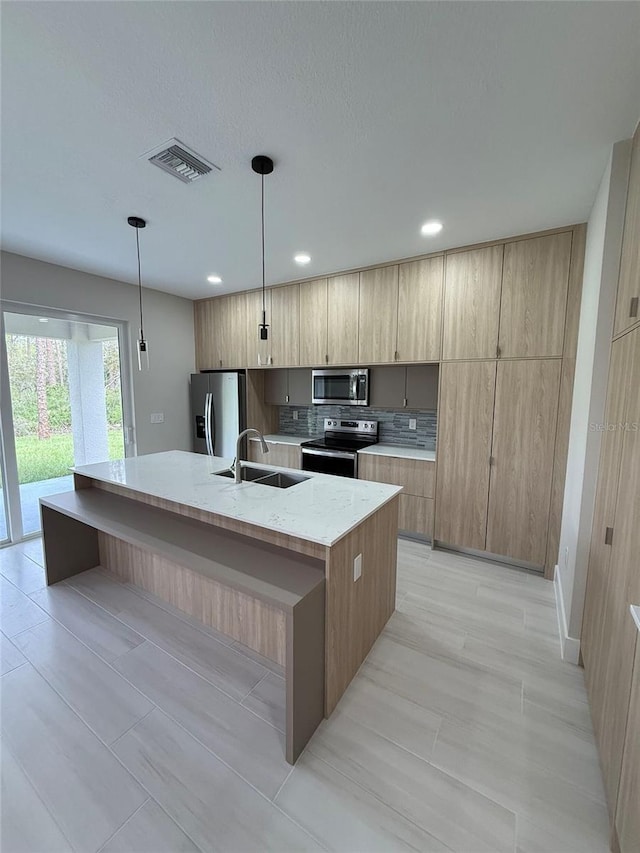 kitchen with appliances with stainless steel finishes, decorative light fixtures, tasteful backsplash, an island with sink, and sink