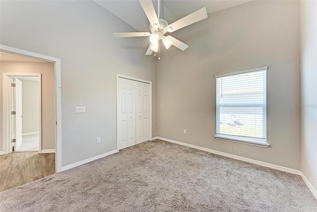 unfurnished bedroom with carpet flooring, a closet, high vaulted ceiling, and ceiling fan