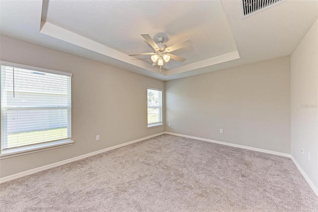 unfurnished room with ceiling fan, light colored carpet, and a tray ceiling