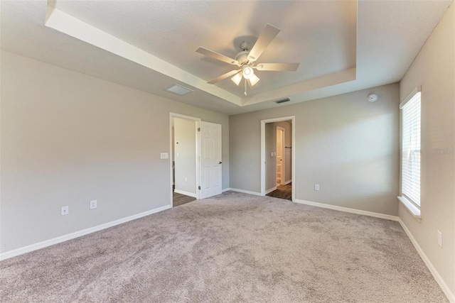 carpeted spare room featuring a raised ceiling, a wealth of natural light, and ceiling fan