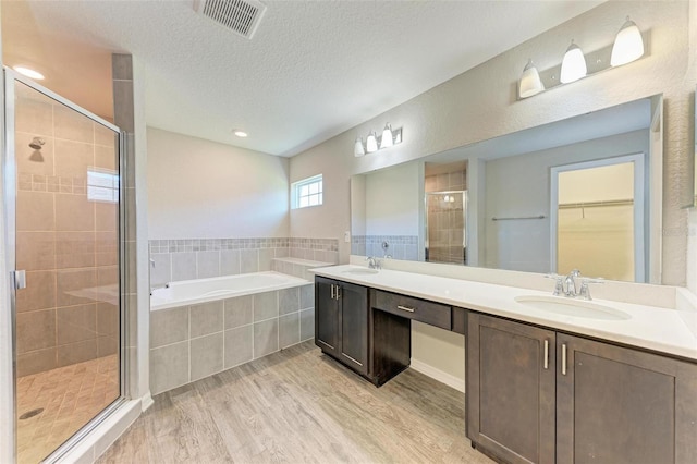 3030 58th Way E, Palmetto, FL 34221 - bathroom with wood finished floors, a stall shower, a garden tub, double vanity, and a textured ceiling