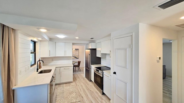 kitchen featuring sink, backsplash, light hardwood / wood-style floors, white cabinets, and appliances with stainless steel finishes