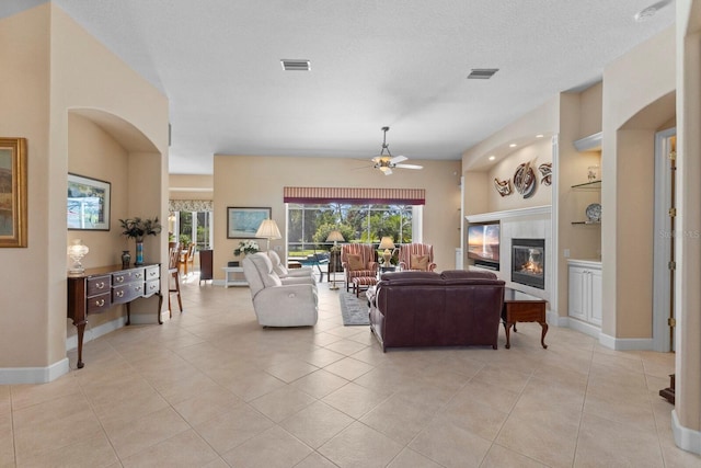 tiled living room featuring a textured ceiling, ceiling fan, and a fireplace