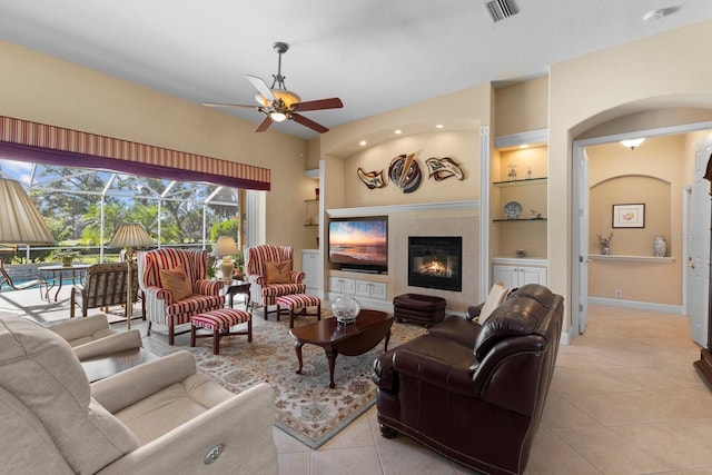 living room featuring a tile fireplace, ceiling fan, built in features, and light tile patterned flooring