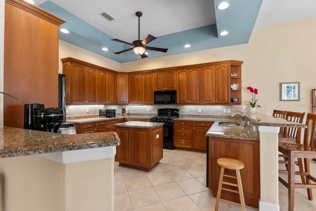 kitchen featuring kitchen peninsula, backsplash, light stone counters, a breakfast bar, and black appliances