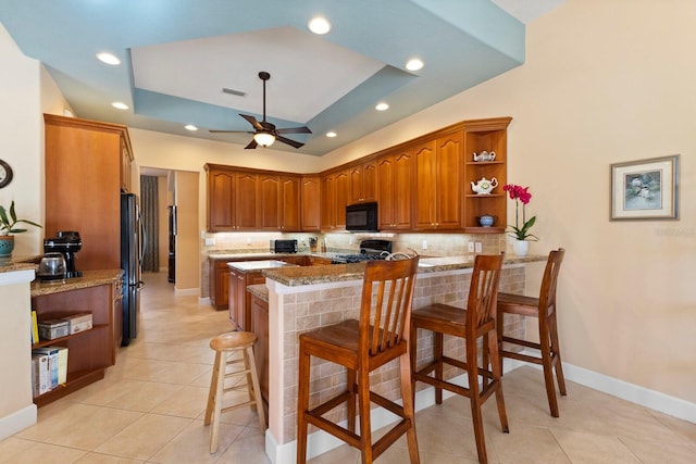 kitchen with kitchen peninsula, tasteful backsplash, a breakfast bar, a raised ceiling, and black appliances