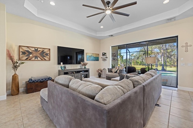 tiled living room with ceiling fan and a raised ceiling