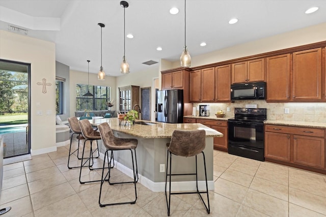 kitchen featuring an island with sink, a breakfast bar area, hanging light fixtures, light stone counters, and black appliances