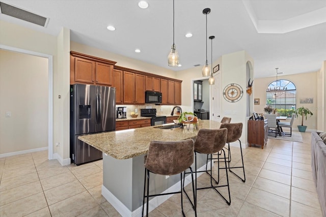 kitchen with light tile patterned floors, a kitchen bar, an island with sink, and black appliances