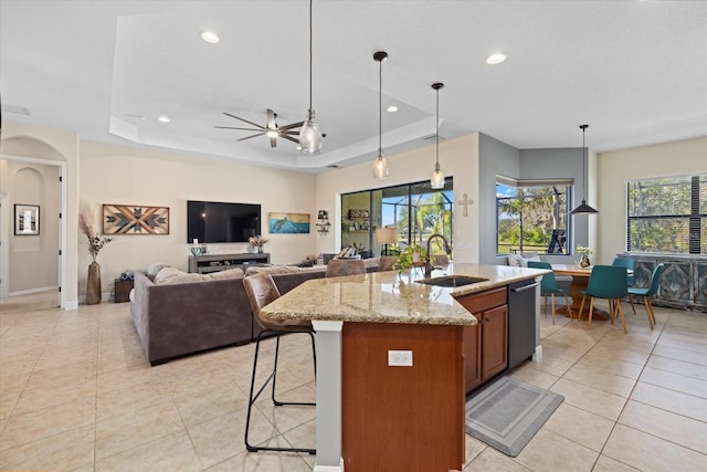 kitchen featuring pendant lighting, sink, light stone counters, a tray ceiling, and a center island with sink