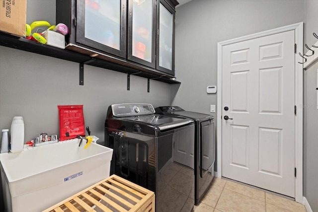 clothes washing area with cabinets, sink, light tile patterned floors, and washer and clothes dryer