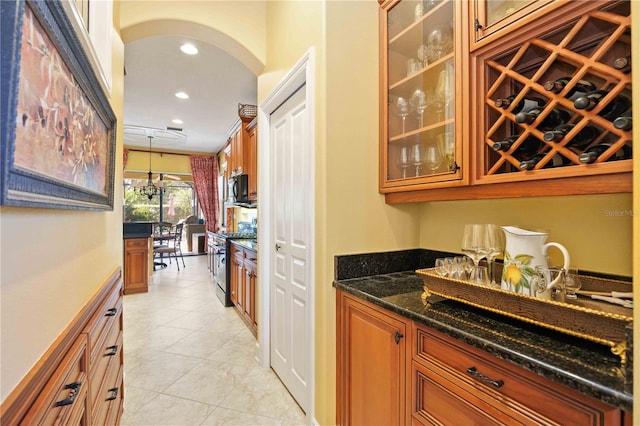 bar featuring dark stone countertops, light tile patterned flooring, decorative light fixtures, and stainless steel range oven