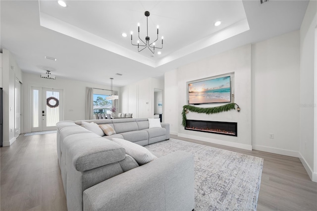 living room with a raised ceiling, light hardwood / wood-style floors, and an inviting chandelier