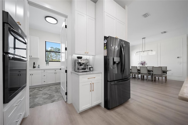 kitchen with light wood-type flooring, black double oven, pendant lighting, stainless steel fridge with ice dispenser, and white cabinetry