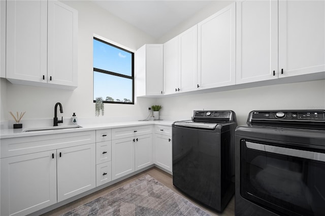 laundry room featuring washing machine and clothes dryer, sink, cabinets, and light hardwood / wood-style flooring