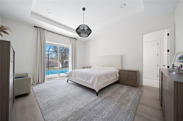 bedroom featuring access to outside, a raised ceiling, and light hardwood / wood-style floors