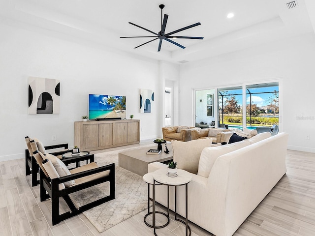 living room with light wood-type flooring, a tray ceiling, and ceiling fan