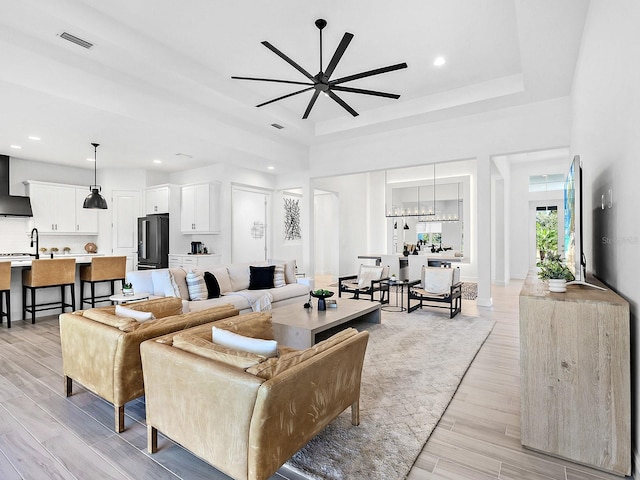 living room featuring a raised ceiling, ceiling fan, and light hardwood / wood-style flooring