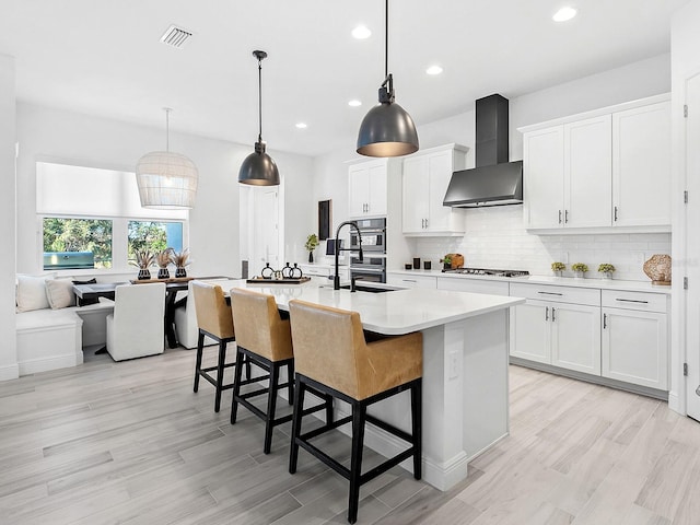 kitchen with white cabinets, wall chimney exhaust hood, a kitchen island with sink, and stainless steel gas stovetop