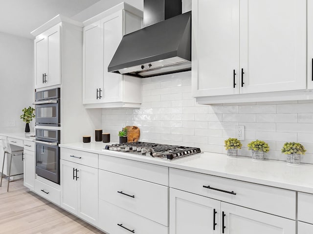 kitchen featuring white cabinetry, light hardwood / wood-style flooring, stainless steel appliances, and wall chimney range hood