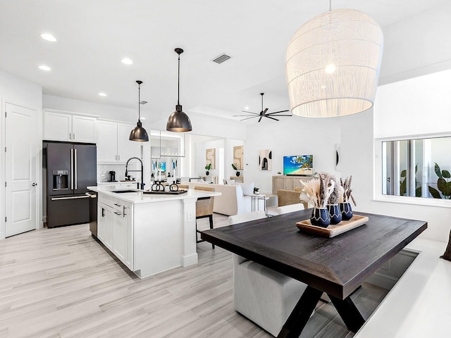 kitchen with stainless steel fridge, hanging light fixtures, white cabinets, and a kitchen island with sink