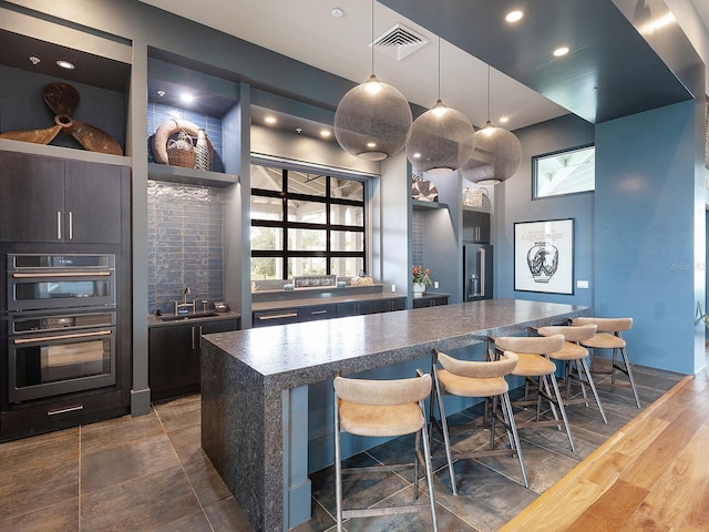 kitchen featuring a center island, dark wood-type flooring, hanging light fixtures, stainless steel double oven, and a breakfast bar area