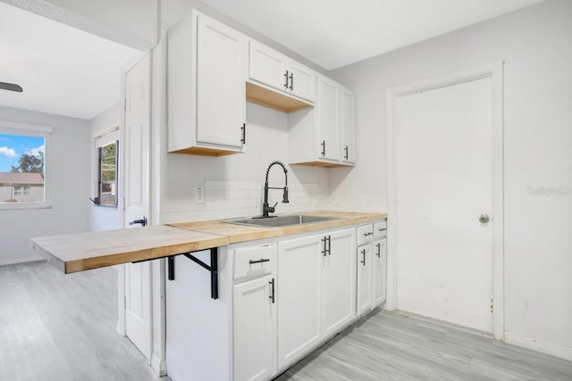 kitchen featuring sink, light hardwood / wood-style flooring, a breakfast bar, white cabinets, and decorative backsplash