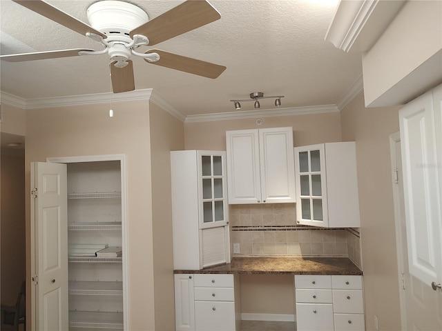 kitchen with white cabinets, ceiling fan, decorative backsplash, built in desk, and ornamental molding