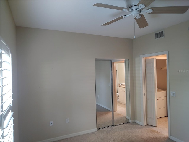 unfurnished bedroom featuring light carpet, ensuite bath, ceiling fan, washer / dryer, and a closet