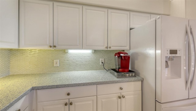 kitchen with tasteful backsplash, white refrigerator with ice dispenser, white cabinets, and light stone counters