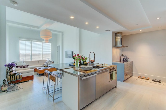 kitchen with dishwasher, a breakfast bar, a kitchen island with sink, sink, and wall chimney exhaust hood