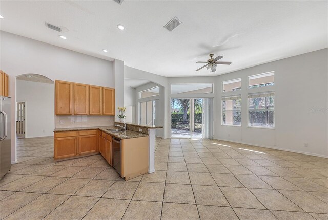 kitchen featuring kitchen peninsula, appliances with stainless steel finishes, ceiling fan, light tile patterned floors, and dark stone countertops