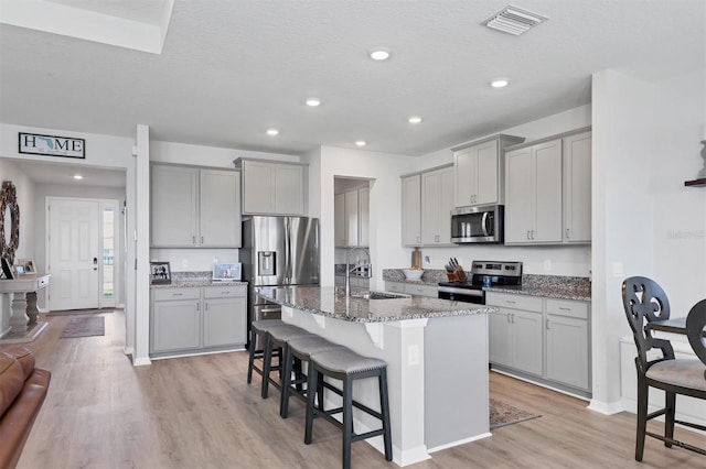 kitchen with gray cabinetry, dark stone counters, a breakfast bar, stainless steel appliances, and an island with sink