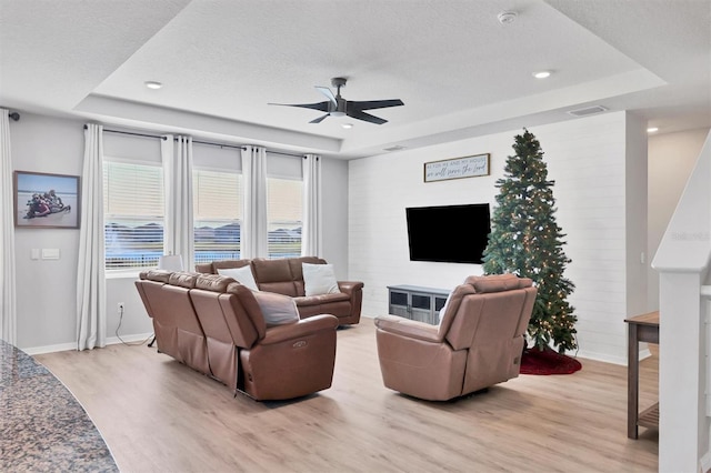 living room featuring a tray ceiling, ceiling fan, and light wood-type flooring