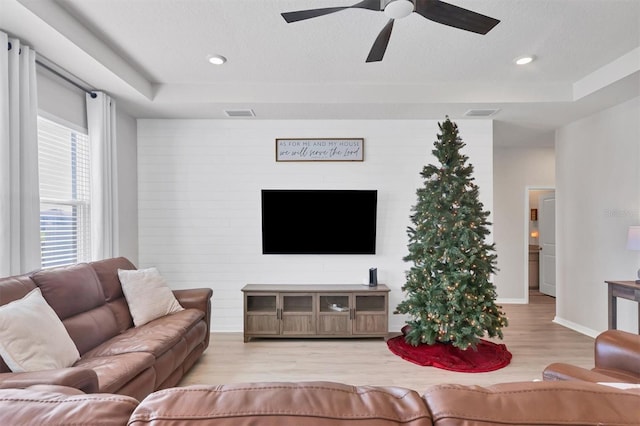 living room featuring light wood-type flooring, a raised ceiling, and ceiling fan