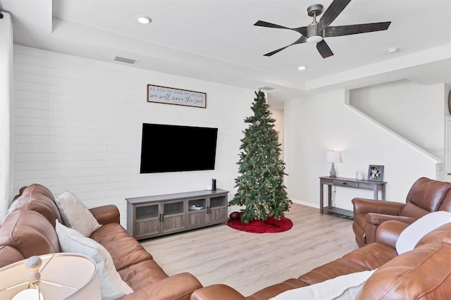 living room featuring ceiling fan, light wood-type flooring, and a tray ceiling