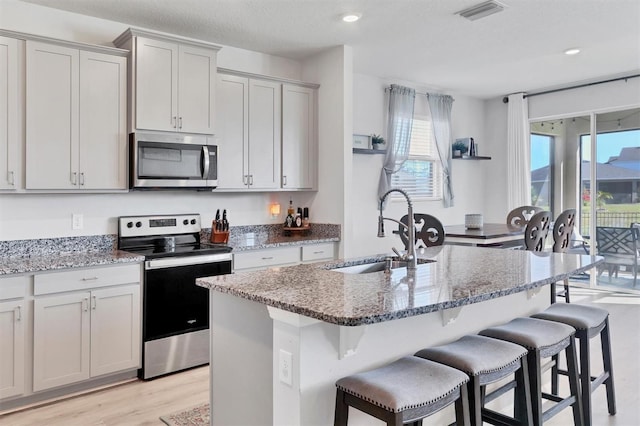 kitchen featuring a kitchen island with sink, sink, stainless steel appliances, and light stone counters