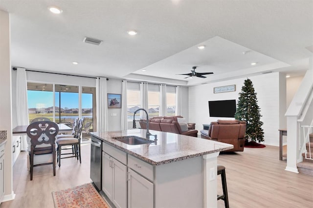 kitchen with ceiling fan, sink, light stone counters, a kitchen island with sink, and light wood-type flooring