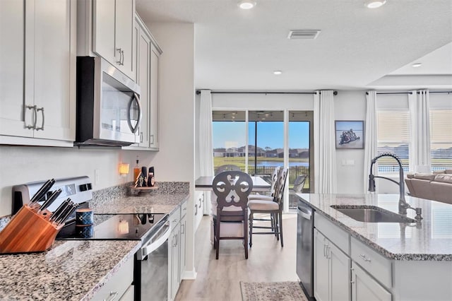 kitchen with sink, light stone counters, light hardwood / wood-style flooring, a textured ceiling, and appliances with stainless steel finishes