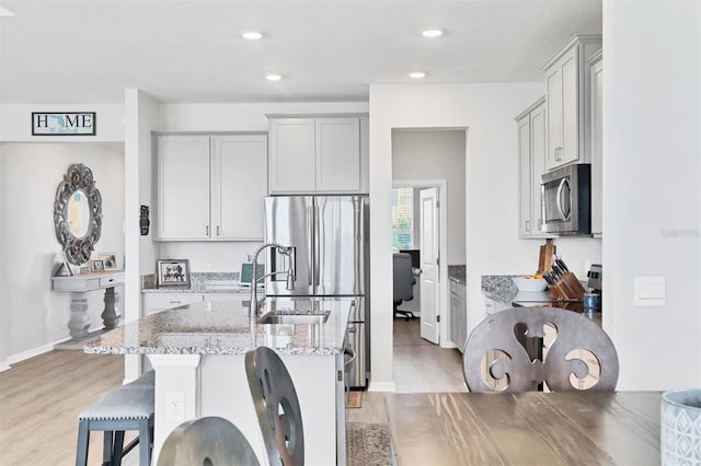 kitchen featuring a kitchen bar, appliances with stainless steel finishes, light stone counters, a kitchen island with sink, and light hardwood / wood-style floors