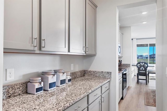 kitchen featuring gray cabinetry, light stone countertops, light wood-type flooring, and appliances with stainless steel finishes