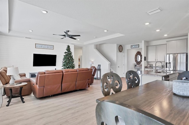 dining space with light wood-type flooring, a textured ceiling, a tray ceiling, ceiling fan, and sink