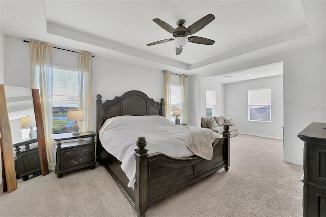 bedroom featuring light carpet, multiple windows, a raised ceiling, and ceiling fan