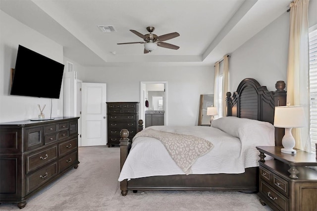 bedroom featuring a tray ceiling, ensuite bath, ceiling fan, and light colored carpet